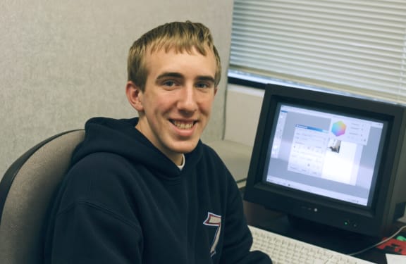 Mike Johnstone seated beside a desktop computer at InfoStar while in high school.